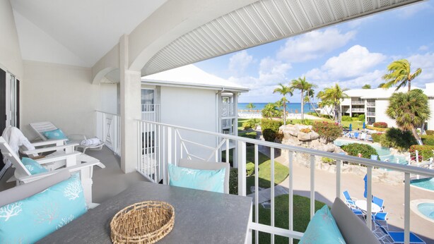 Ein Balkon mit weißer Möbel, Blick auf den Strand und ein Poolbereich.