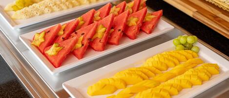 A buffet with various fruits and vegetables arranged on white trays.