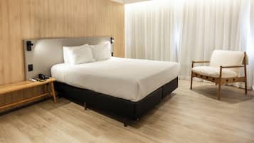 Quarto de hotel moderno com uma cama grande, uma mesinha de cabeceira de madeira, uma cadeira e um painel de parede de madeira.