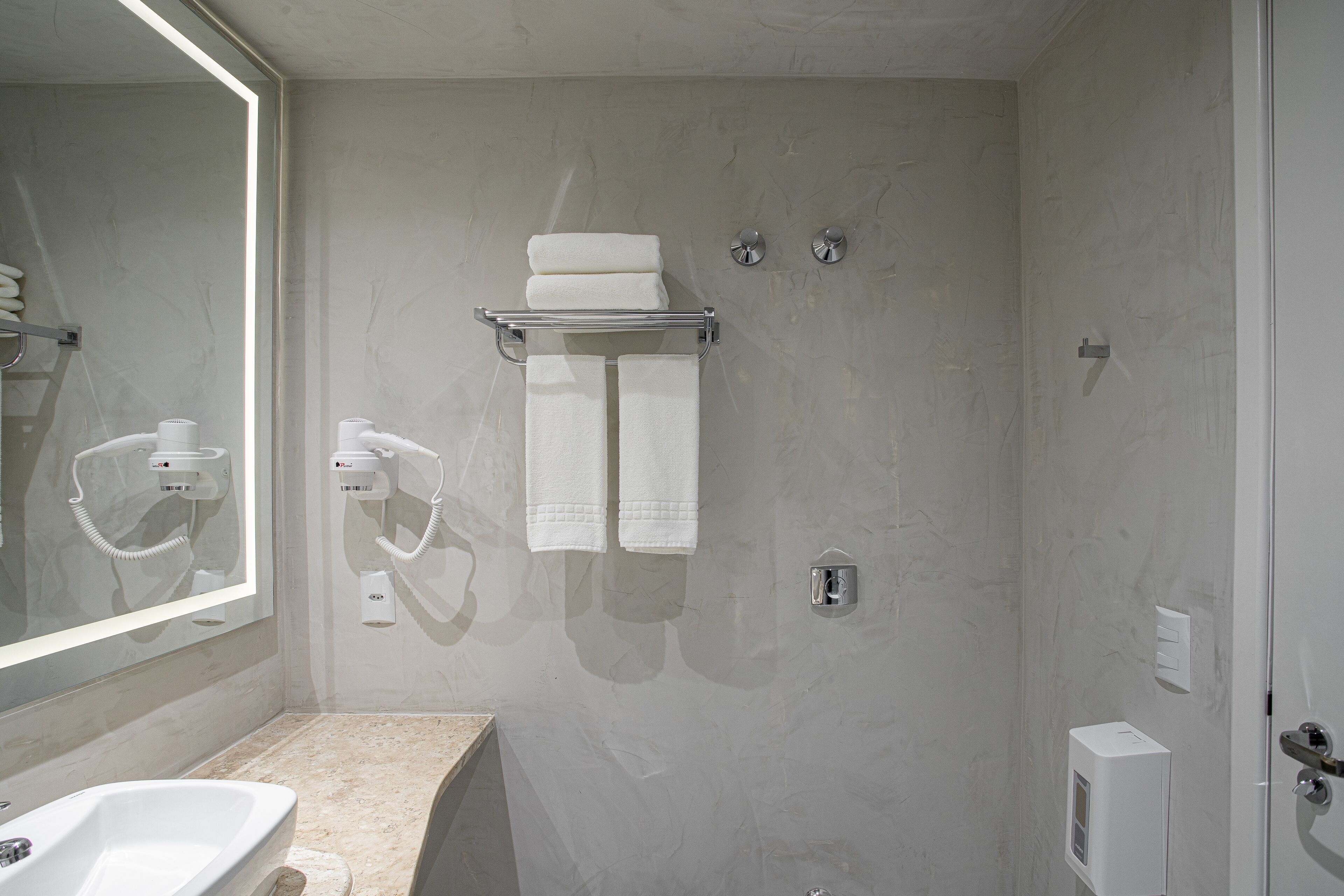 Een moderne badkamer met een grote spiegel, een wastafel, een handdoekrek met opgevouwen handdoeken en een douchegedeelte.