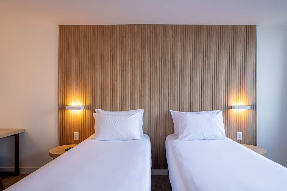 Two single beds with white linens, a wooden slat wall, and two bedside lamps.