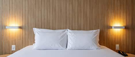 A neatly made bed with white linens, two bedside lamps, and a wooden slatted headboard.