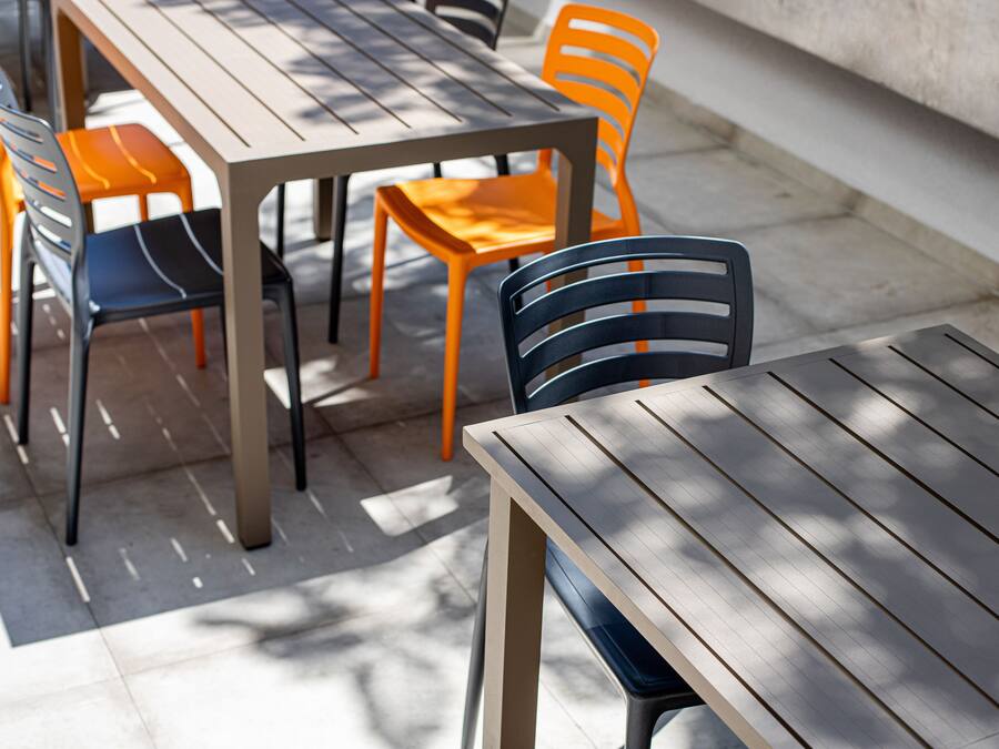 Un comedor con una mesa larga y varias sillas, algunas con cojines anaranjados.