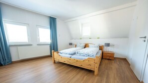 Une chambre à coucher avec un lit en bois, une table de chevet, une commode et une fenêtre avec des rideaux.