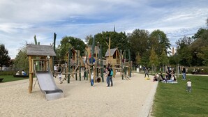 Un terrain de jeux doté de diverses structures ludiques, notamment un toboggan et des zones d’escalade, le tout entouré de sable et d’herbe.