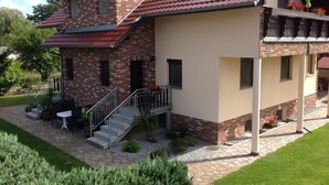Une maison à deux étages avec un toit recouvert de tuiles rouges, un balcon orné de fleurs rouges et un petit espace extérieur aménagé avec une table et des chaises.
