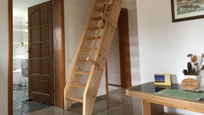 Une échelle en bois appuyée contre un mur dans une pièce où se trouvent une porte et un tableau encadré.