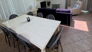 Ein geräumiger Essbereich mit einem weißen Tisch, karierten Stühlen, einem Kamin und einem an der Wand befestigten Fernseher.