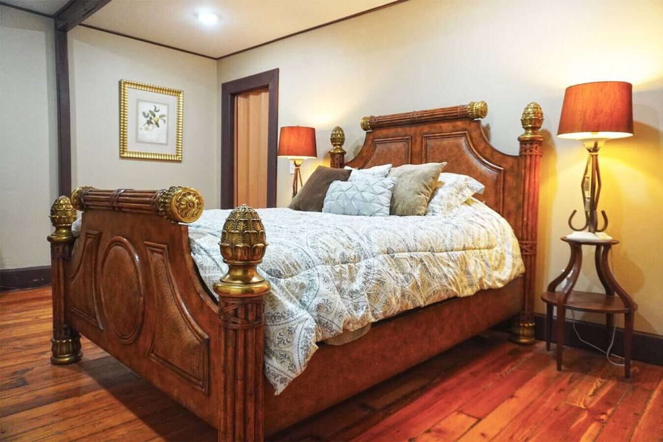 Un lit à baldaquin en bois, agrémenté d’une couvre-lit à motifs et de plusieurs coussins, avec deux lampes de chevet de chaque côté.