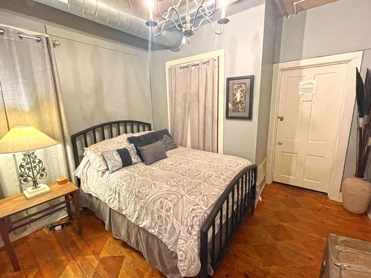 A bedroom with a bed, a nightstand, a lamp, a door, and a wall-mounted picture.