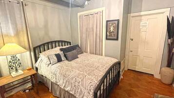 A bedroom with a bed, a nightstand, a lamp, a door, and a wall-mounted picture.