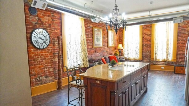 A spacious kitchen with a large island, brick walls, and a chandelier. - Shopping District Apt | Heart of Historic Downtown (Marietta)