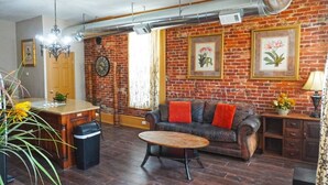 A cozy living room with a brick wall, a leather sofa, a wooden coffee table, and a dining area with a bar. - Shopping District Apt | Heart of Historic Downtown (Marietta)