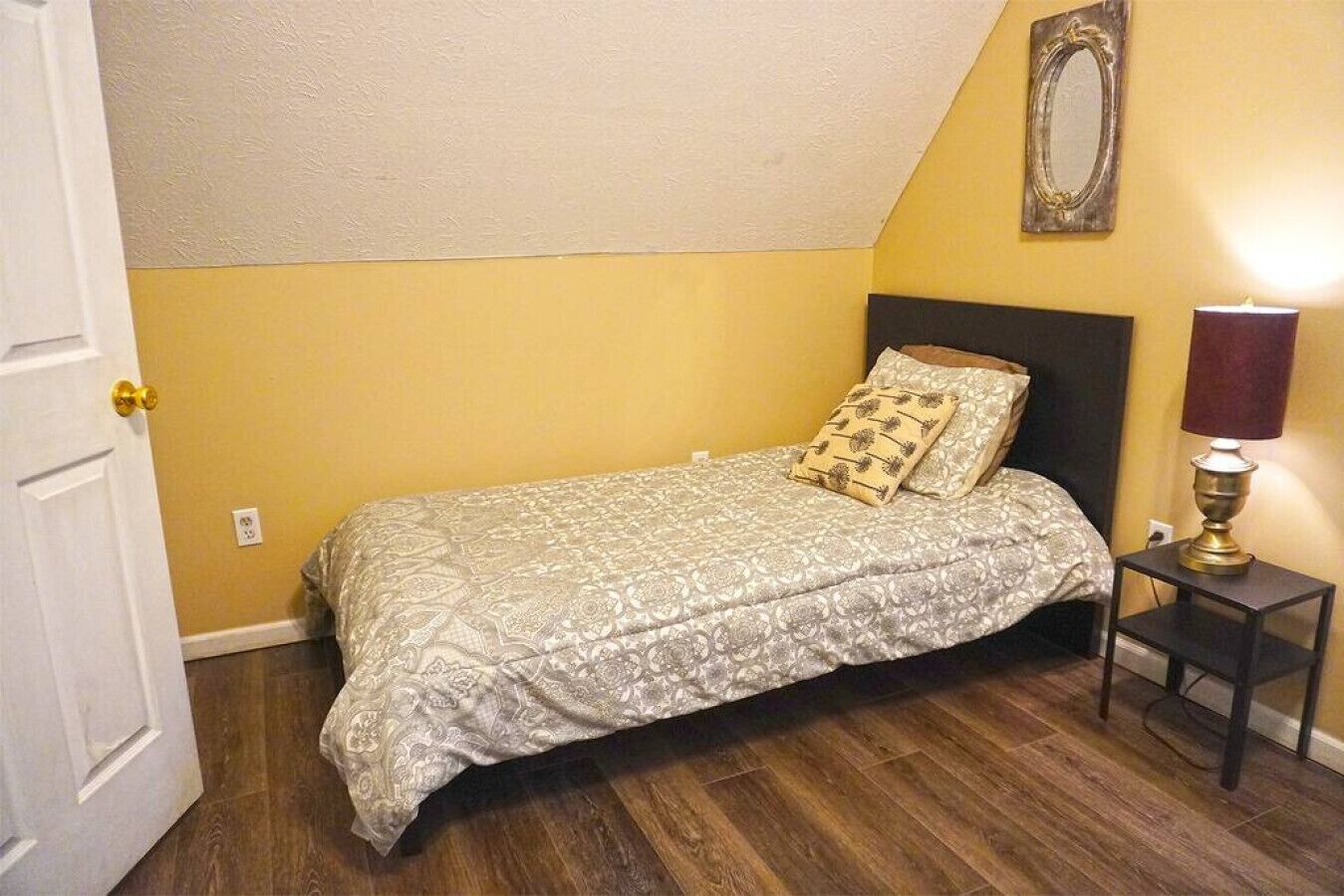 A bedroom with a bed, a nightstand, a lamp, and a mirror on the wall.
