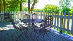 Eine überdachte Terrasse im Freien mit einem runden Tisch und Stühlen, umgeben von einem weißen Zierzaun.