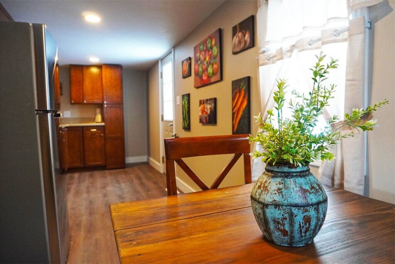 Una cocina con armarios de madera, una mesa de comedor con un florero de plantas verdes y obras de arte en las paredes.