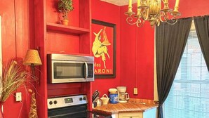 Une cuisine de taille réduite avec des murs rouges, un four à micro-ondes, une cuisinière et un évier. Un lustre est suspendu au-dessus du comptoir.