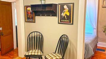 Una habitación con dos sillas de madera con cojines estampados, un estante empotrado con dos cuadros enmarcados, una lámpara colgante y una puerta que da a otra estancia.