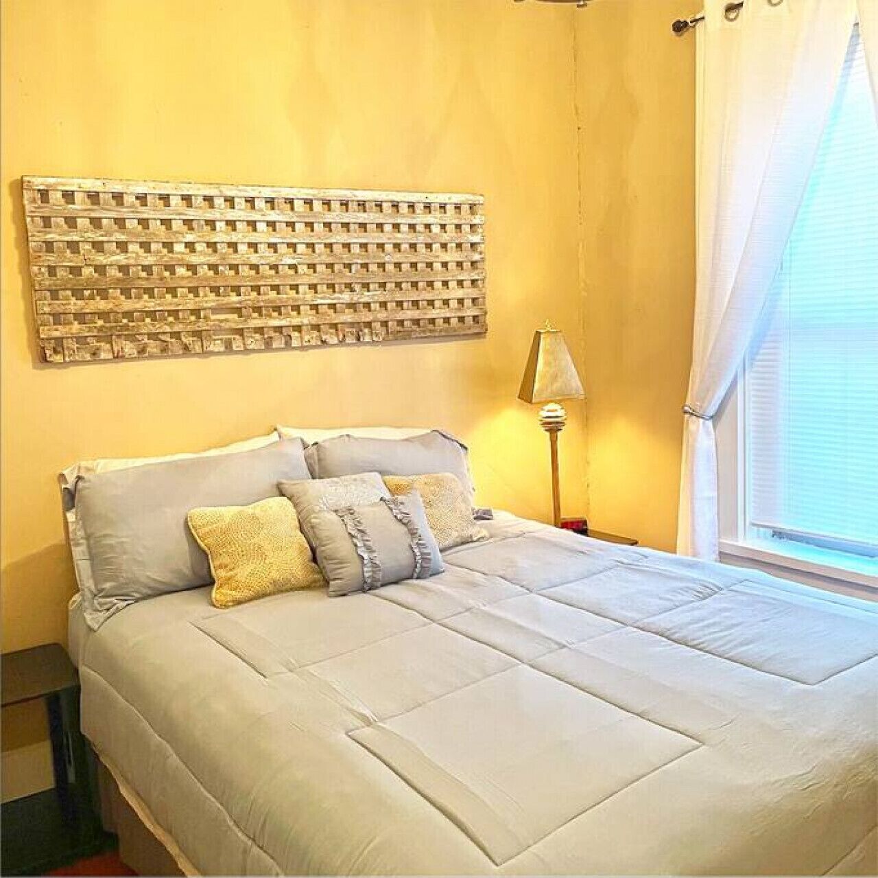 Une chambre à coucher avec un lit, des oreillers, une lampe et une œuvre d’art accrochée au mur.