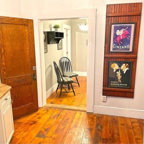 Enter a room with a wooden floor, featuring framed posters and a comfortable chair with a checkered cushion.