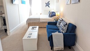 A bedroom with a bed, a blue sofa, a white coffee table, and a TV on the wall.