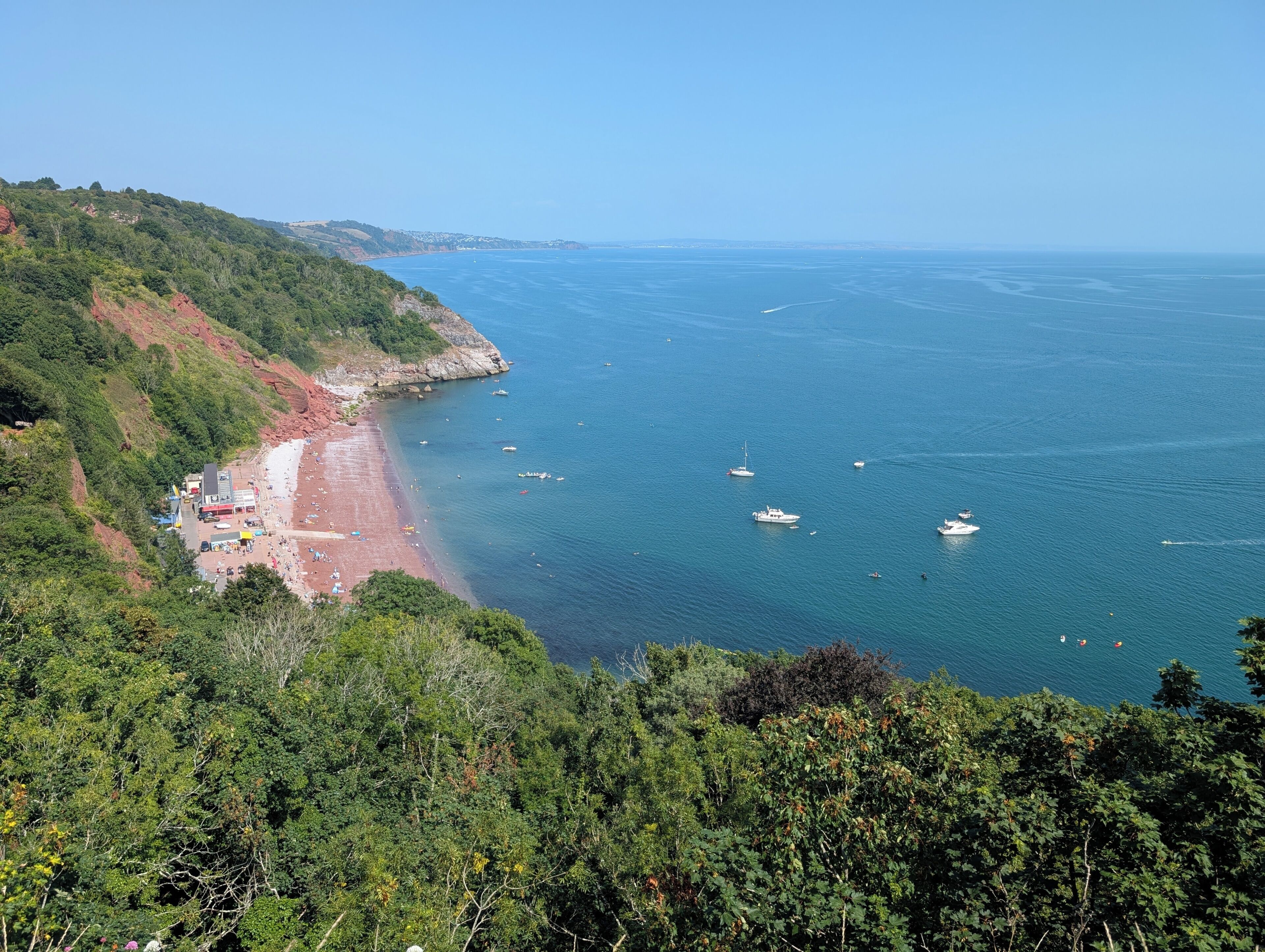 A coastal view with a beach, boats, and a forested hillside.