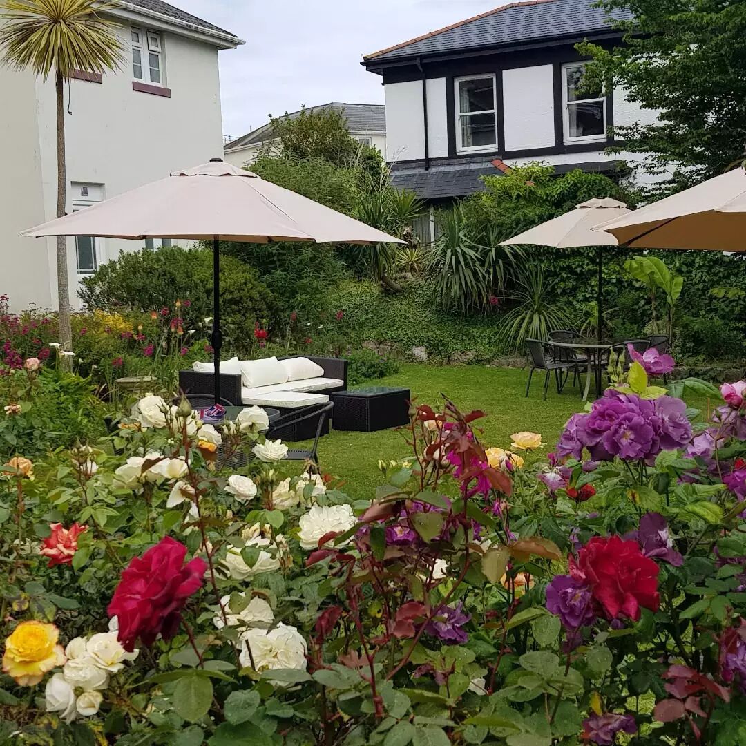 Un jardín con diversas flores y una zona de estar con mobiliario de exterior.