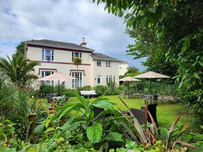 A large house with a garden patio area featuring outdoor furniture and umbrellas.
