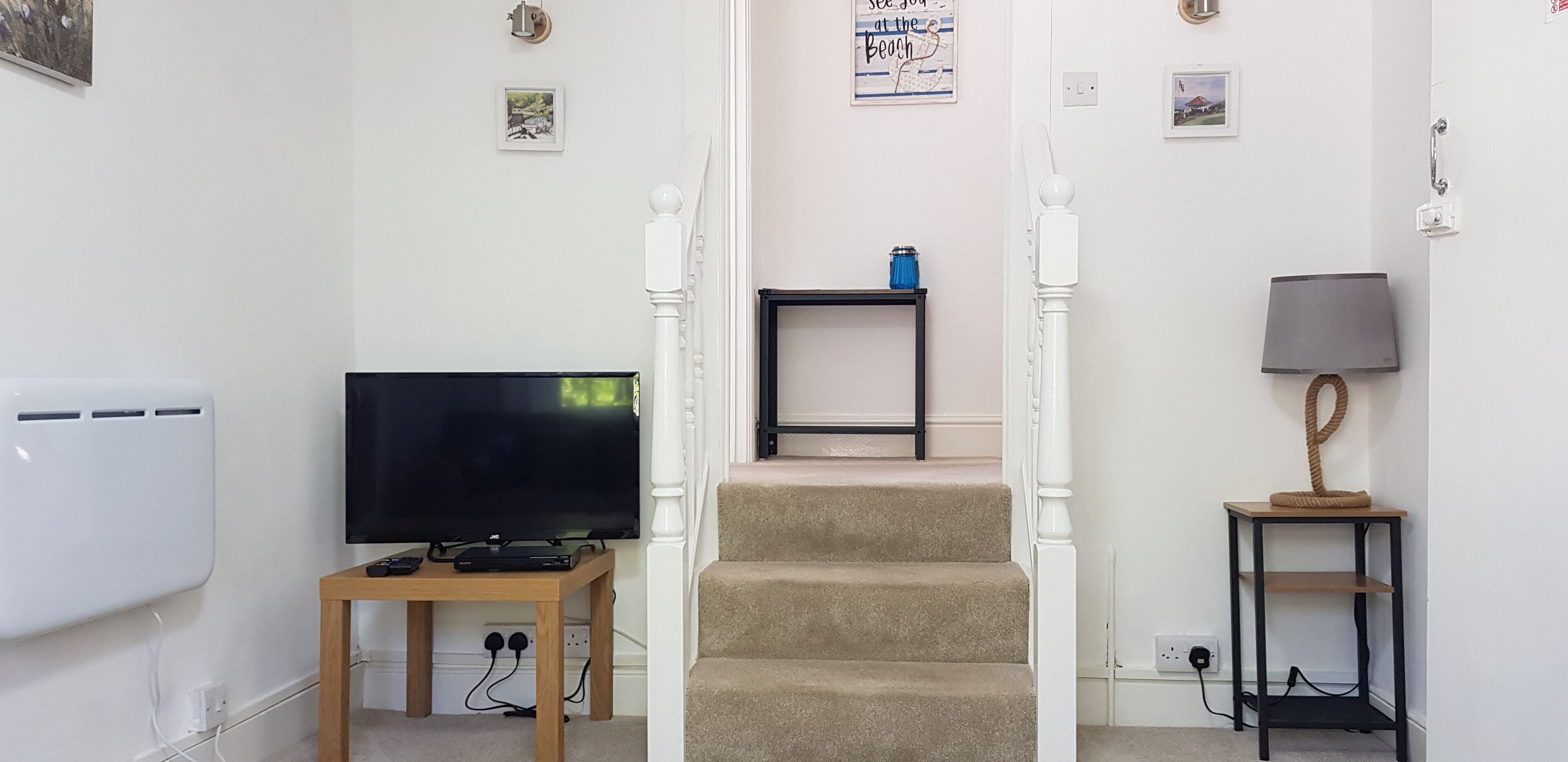 Una escalera que lleva a un dormitorio con televisión, una lámpara y una mesita.