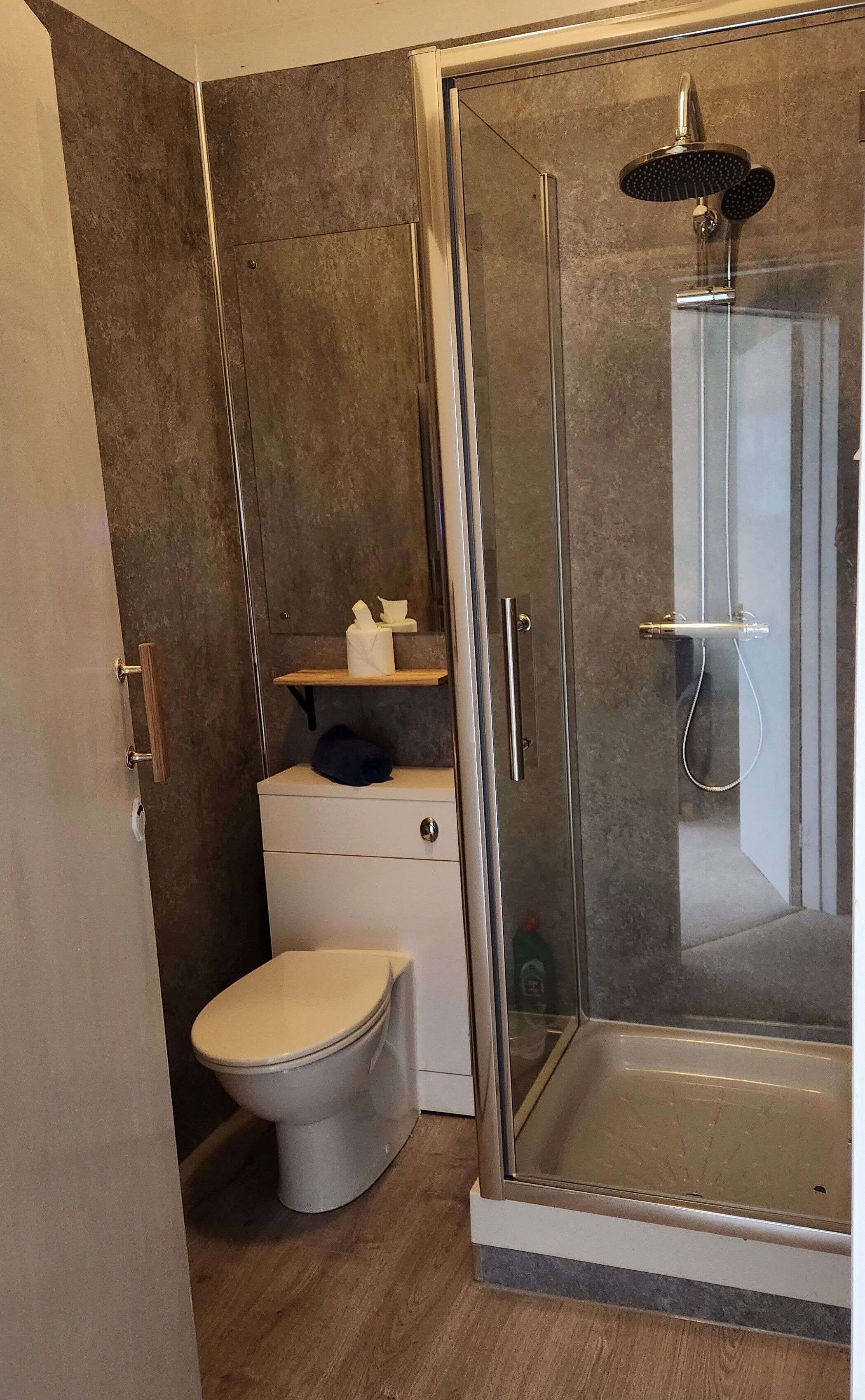 Un baño moderno con ducha de vidrio, inodoro y una pequeña repisa con artículos de aseo.