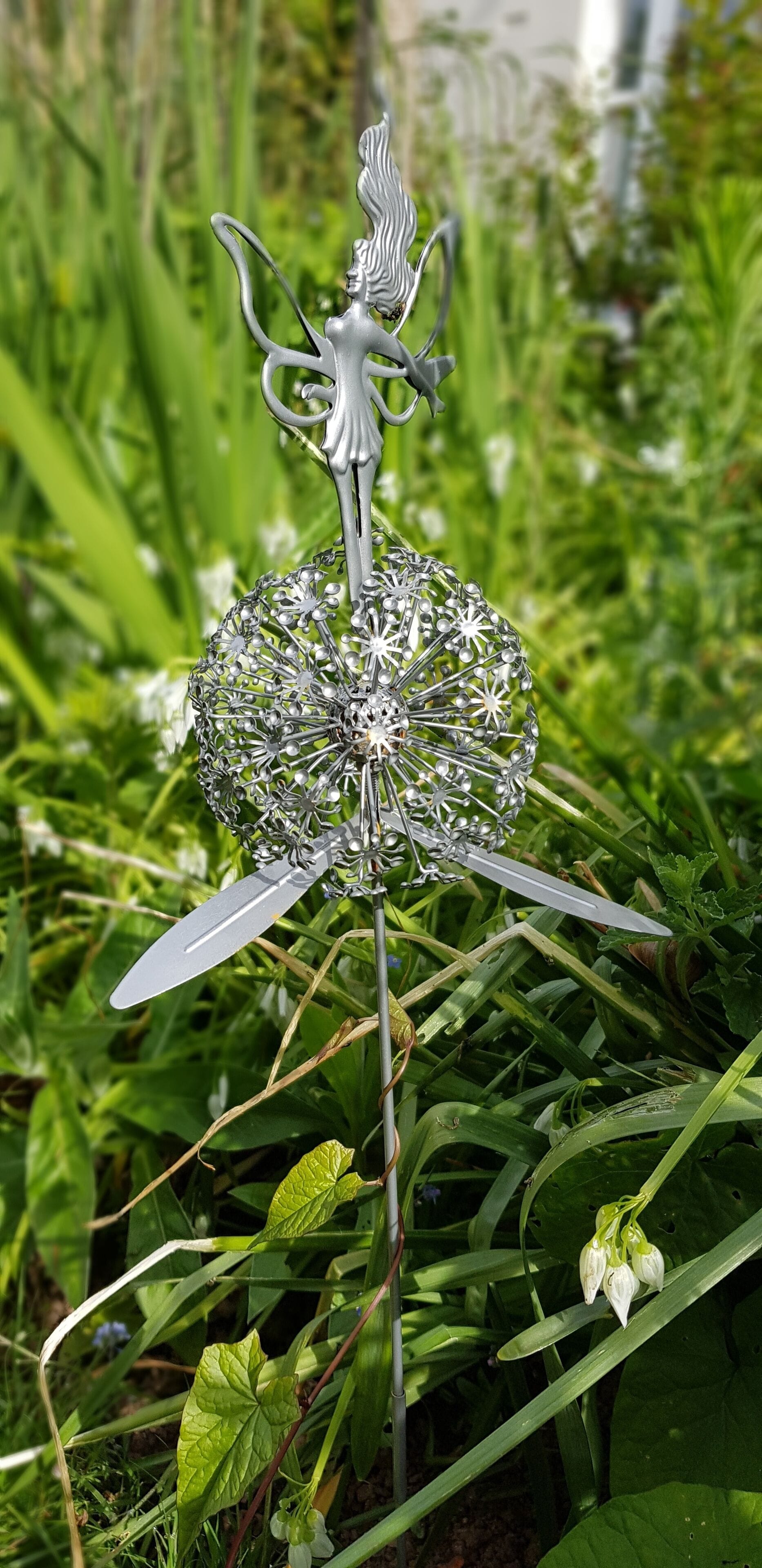A metal sculpture with a figure and a spherical object, set in a garden with green foliage.