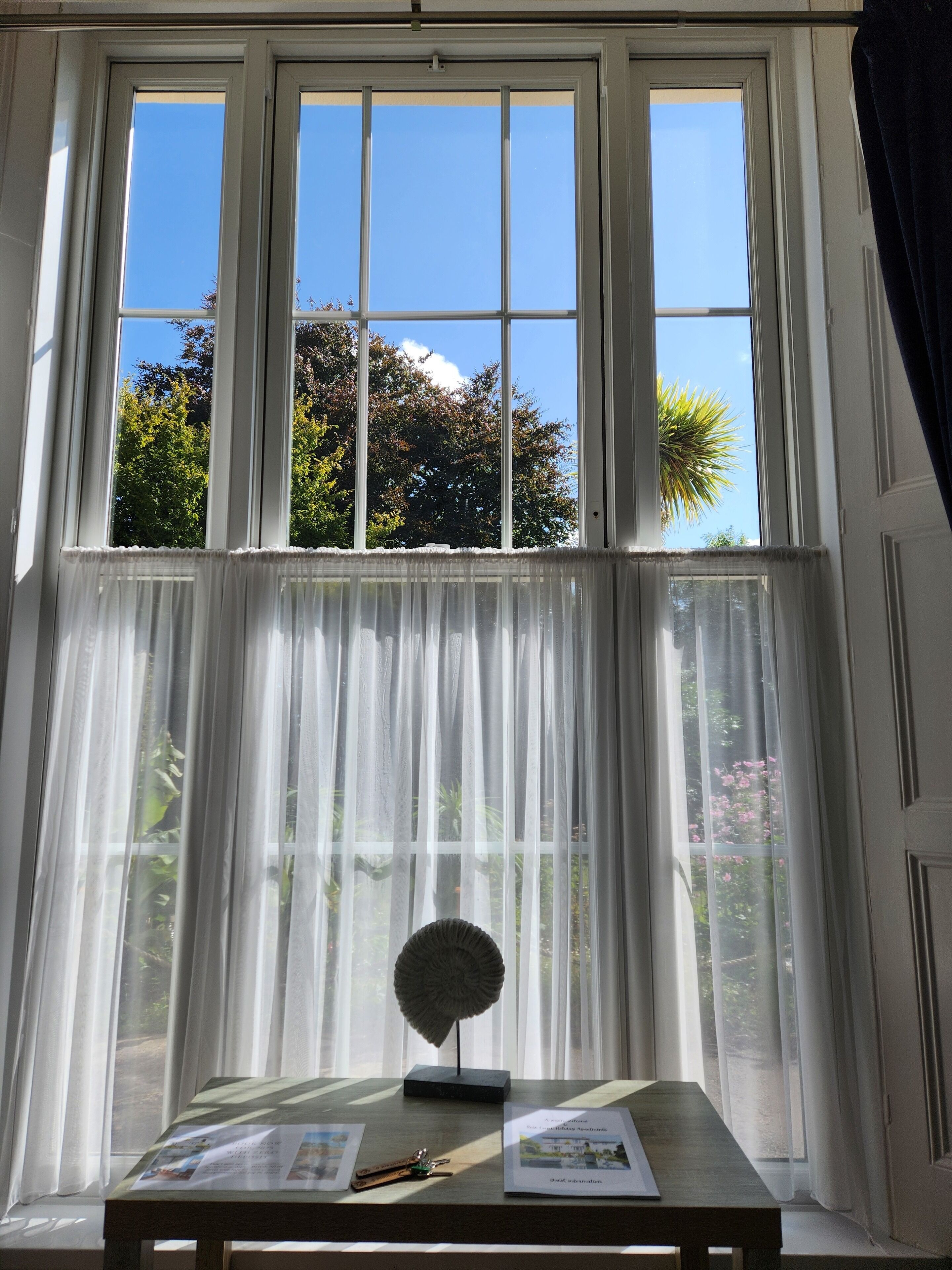 Une pièce dotée d’une grande fenêtre, d’une table agrémentée d’un objet décoratif, et offrant une vue sur les arbres et le ciel.