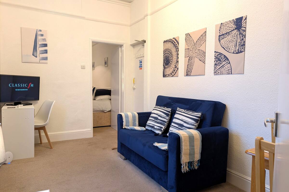 A modern living room with a blue sofa, a flat-screen TV, and artwork on the walls.
