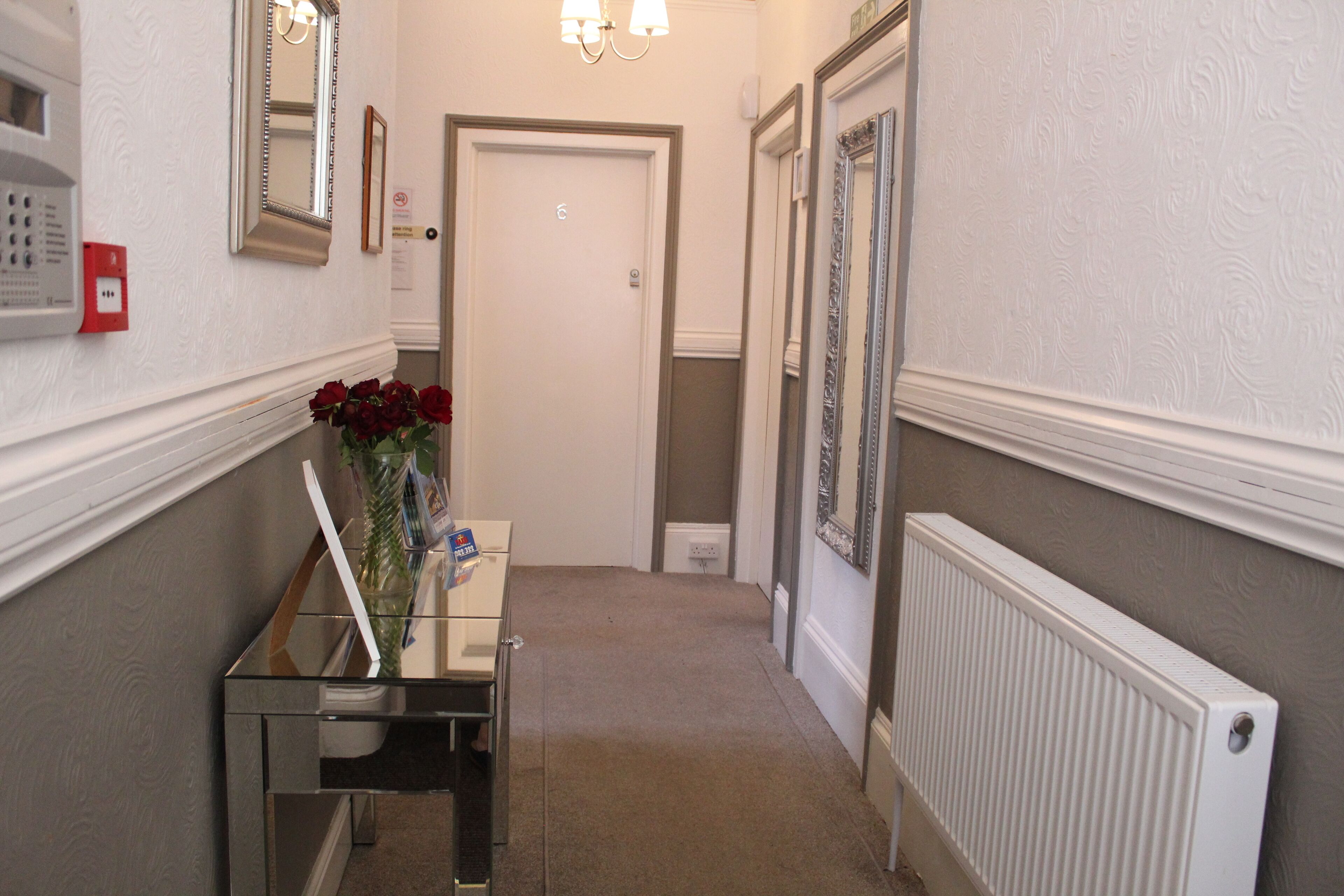 A hallway with a radiator, a door, a mirror, and a small table with a vase of flowers.