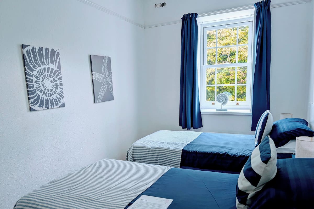 A bedroom with two beds, a window with curtains, and two wall art pieces.