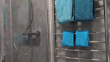 A shower area with a glass door, a chrome showerhead, and a towel rack with two blue towels.
