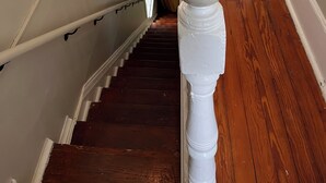 Un escalier en bois, doté de balustrades blanches et d’une main courante, mène à un palier où se trouve un tapis à motifs.