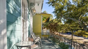 Un balcon avec une table et des chaises, une balustrade et une vue sur la rue et les arbres.
