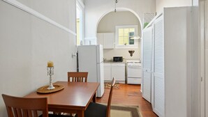 Une cuisine de taille réduite avec des meubles blancs, un réfrigérateur et une cuisinière. On y trouve une table à manger avec des chaises et une bougie.