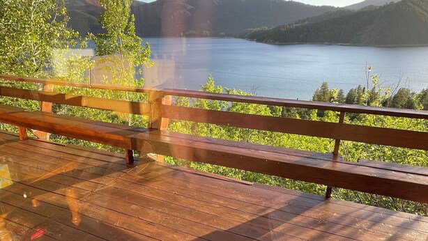 Een houten terras met een reling, met uitzicht op een meer en heuvels.