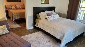 A bedroom with a large bed, a smaller bed in the background, a brown chair, and a patterned rug. - Misty Morn Suite in Cascade Inn at Fall Creek Falls (Pikeville)
