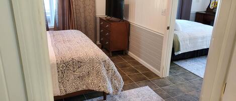 A bedroom with a bed, a dresser, a television, and a bathroom visible through an open door.