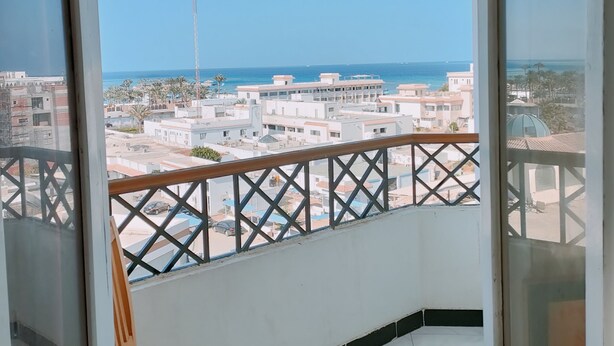 A balcony with a view of a coastal cityscape, a chair, and a tiled floor. - Diana Hotel  (Hurghada)