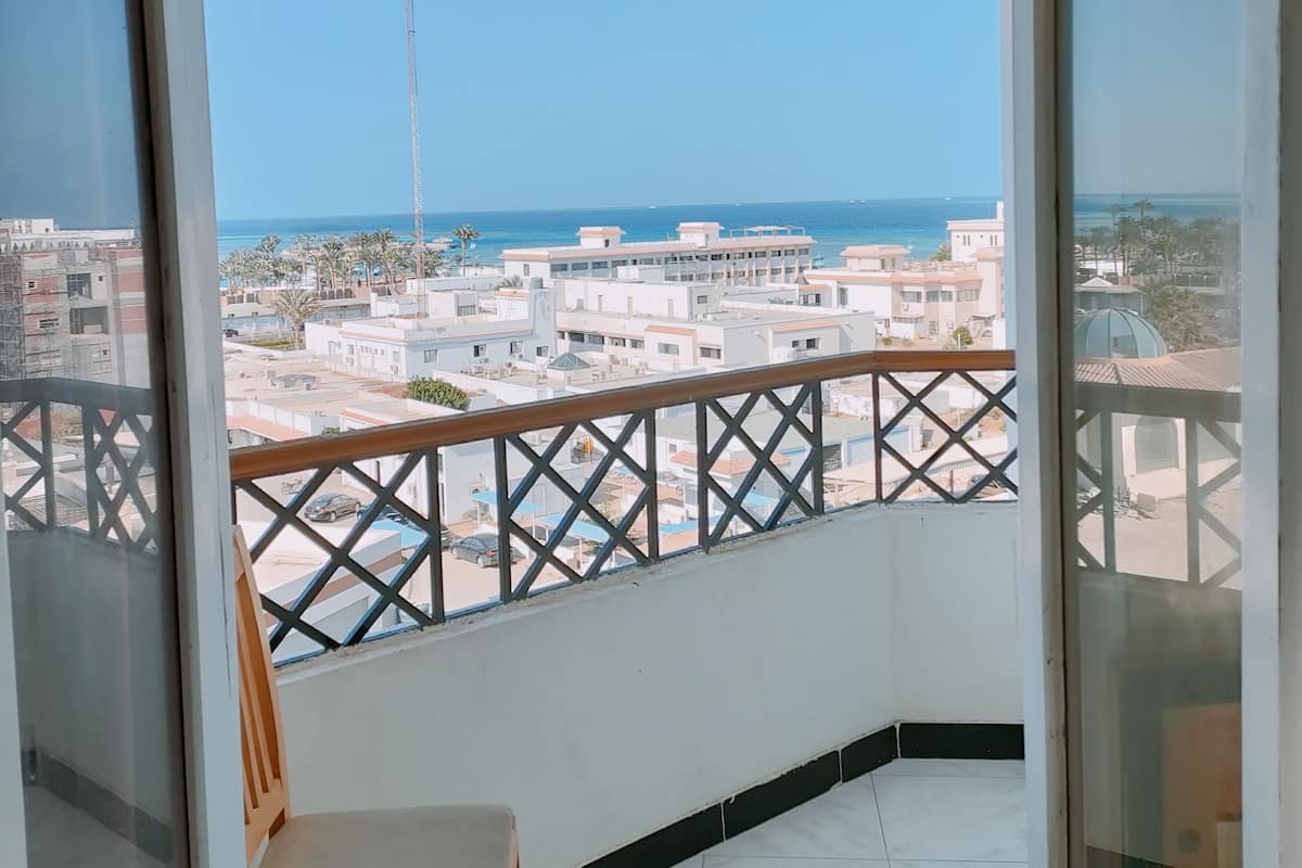 A balcony with a view of a coastal cityscape, a chair, and a tiled floor.