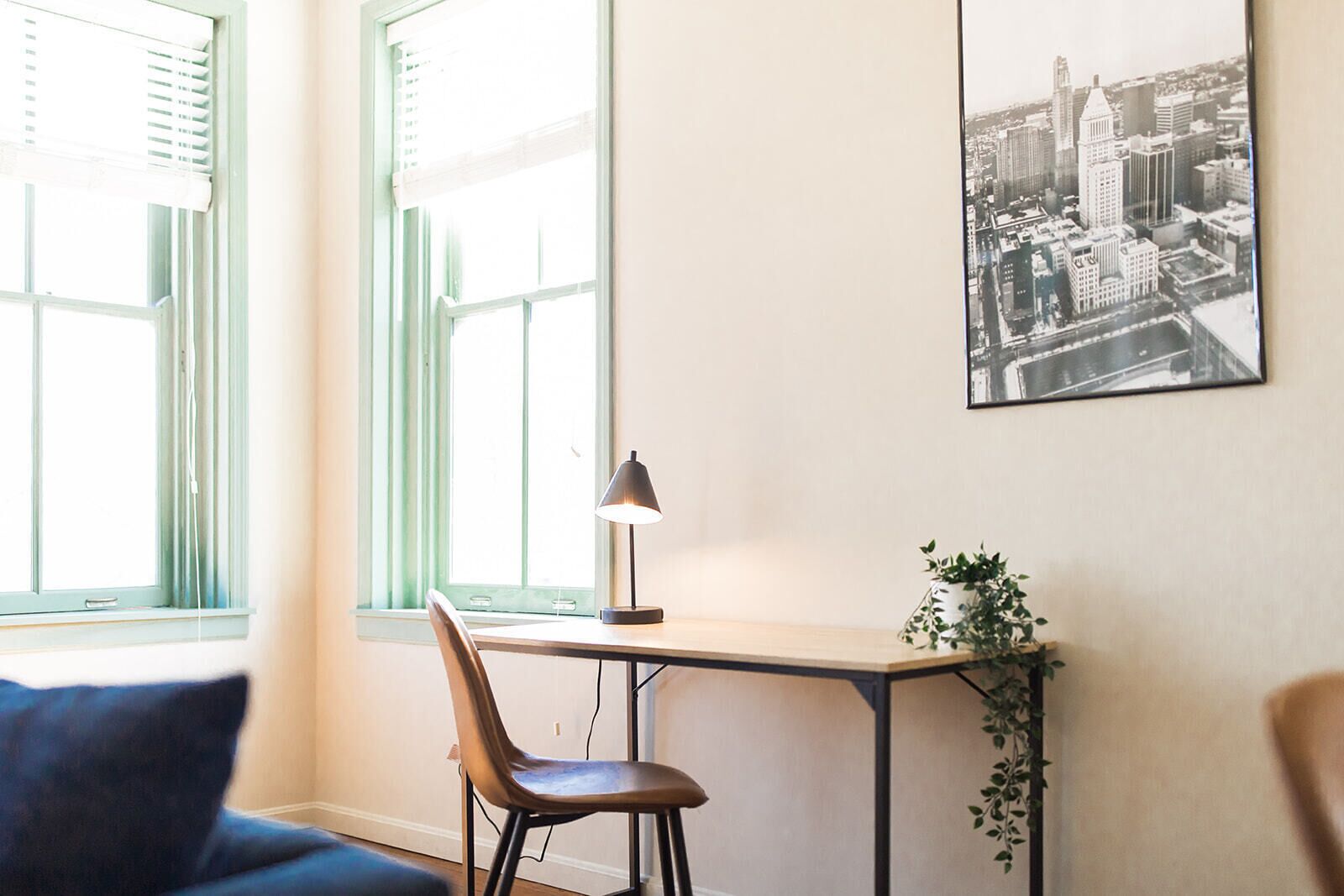 Ein Zimmer mit Schreibtisch, Stuhl und einem Stadtbild in einem Bilderrahmen an der Wand.