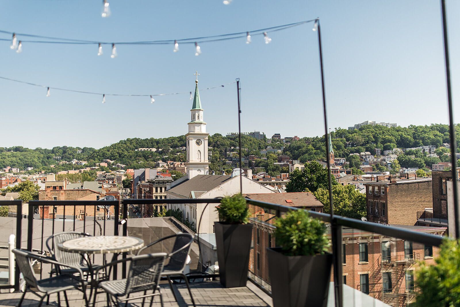 A balcony with outdoor seating, a view of a cityscape, and a church steeple in the background.