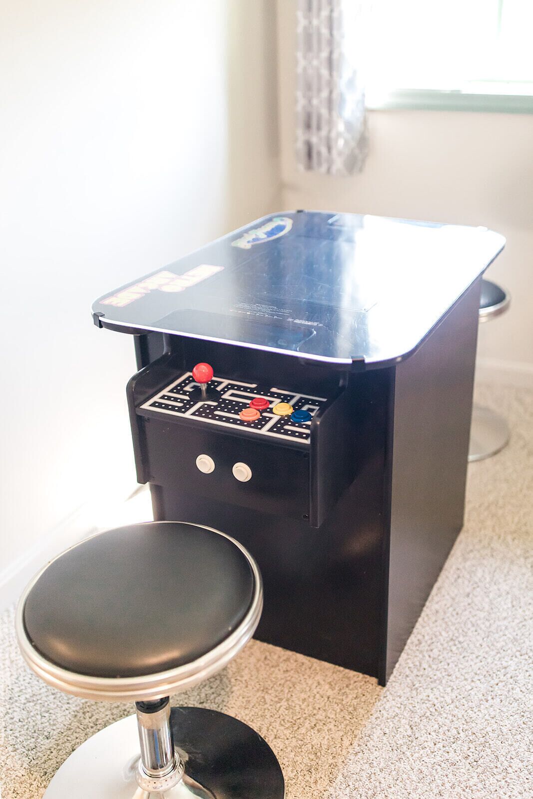 A small, black arcade machine with a stool in front of it.