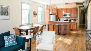 A modern kitchen with wooden cabinets, a central island, and a dining area with a table and chairs. - The Penthouse- Heart of OTR w/Rooftop Terrace (Cincinnati)