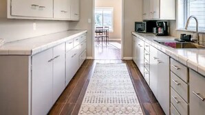 A narrow kitchen with white cabinets, a wooden floor, and a patterned rug.