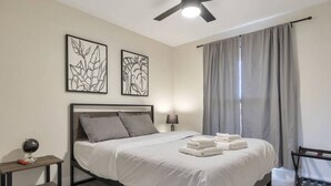 A neatly made bed with white linens, a bedside lamp, and two framed artworks on the wall. - Heated Pool, Quiet Neighborhood (Phoenix)